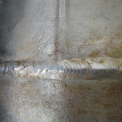 External aspect of the 8" diameter pipe that suffered localized thinning and leakage associated to the welded regions.  The vertical weld is the pipe seam and the horizontal weld is the circunferential butt weld.
