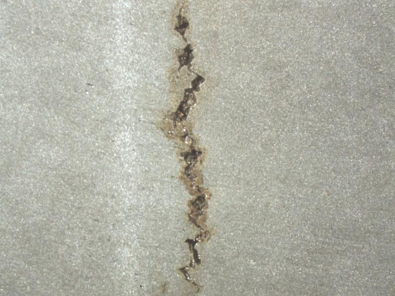 Longitudinal section of the mooring chain at the welded region in a position where the crack did not propagate to the surface yet. It is possible to see the crack parallel to the butt weld and presenting an irregular shape.