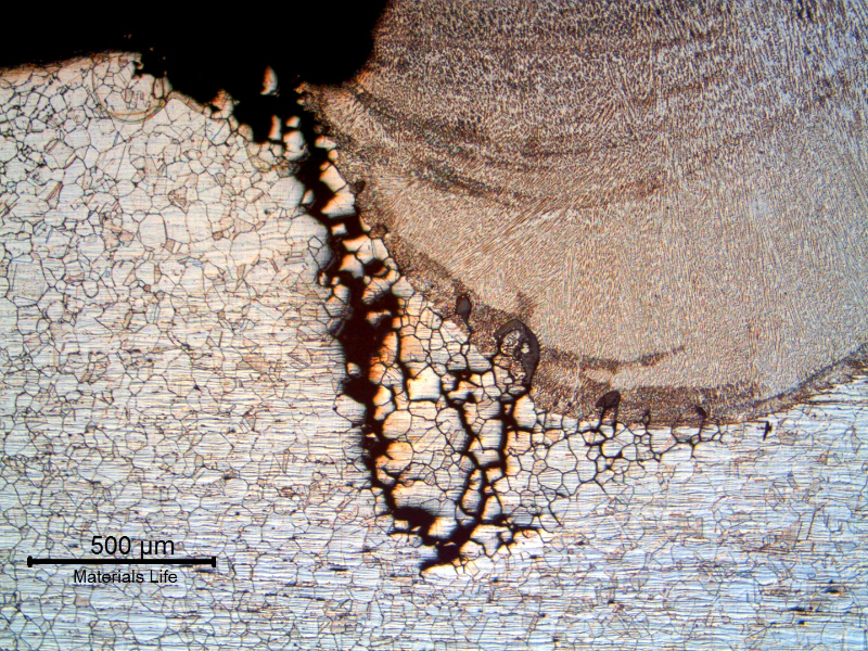 Micrography of a section transverse to the repair weld showing that the macroscopic crack, detected at the surface of the plate, occurred exactly at the margin of the weld bead.  It is possible to see that the bead was deposited over a region that was already corroded (intergranular corrosion) and the macroscopic crack is the opening of several corroded grains.