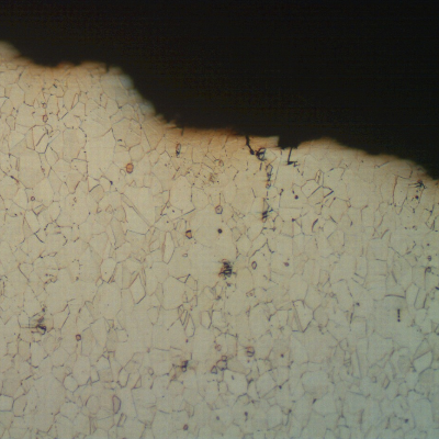 Micrographic aspect of a longitudinal section of the splined shaft, at the fracture surface (top of the figure).  The transgranular fatigue propagation presents shallow secondary cracks at regions of particles in the structure.