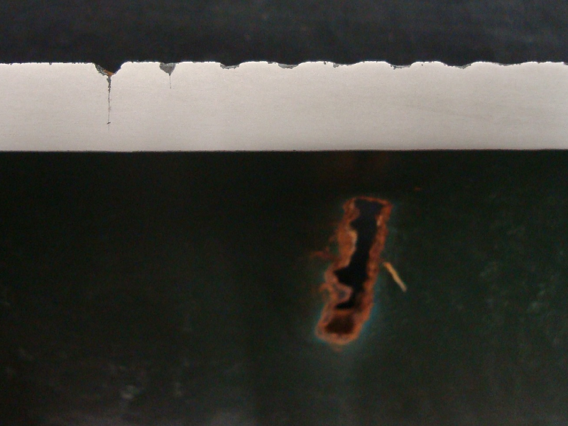 The longitudinal section of the 1/2" thick pipe close to the washout position shows that the external tool marks are like notches that are corroded and cracks are iniciating from the corroded regions. The top of the figure presents the external pipe surface and the bottom of the figure presents the internal pipe surface, with a green coating and the rusted washout.