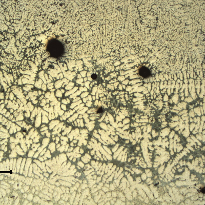 Low magnification micrography of the welded region, showing the base metal in the bottom, the fusion zone (between the liquidus and solidus temperatures) in the center and the weld metal in the top.  There are pores close to the weld metal and in the fusion zone the interdendritic space was melted and the eutectic morphology was changed.