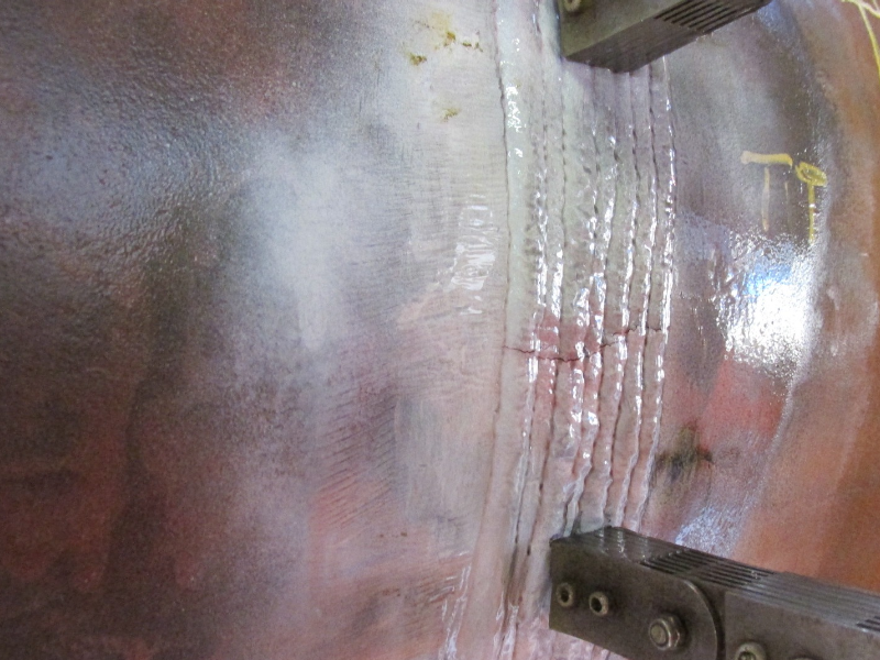 Image of the magnetic particle test, using a white contrast, presenting the cracks at the surface of the weld metal.  The cracks are transverse to the weld and do not propagate into the base metals. A forged T in the right side of the figure and a thick wall tube in the left side of the figure, both in P12 CrMo steel.