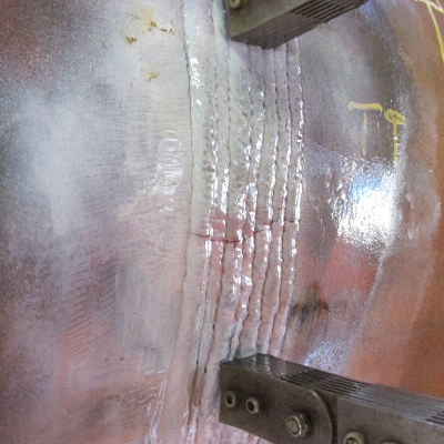 Image of the magnetic particle test, using a white contrast, presenting the cracks at the surface of the weld metal.  The cracks are transverse to the weld and do not propagate into the base metals. A forged T in the right side of the figure and a thick wall tube in the left side of the figure, both in P12 CrMo steel.