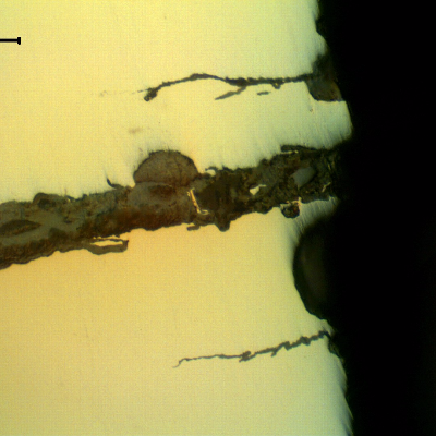 As polished micrography of the external surface of the tubular equipment, close to the fracture position (it is to the top of the figure),  showing corrosion fatigue cracks.  These are multiple cracks, paralel to the main fracture, slightly branched and fully filled with oxides.