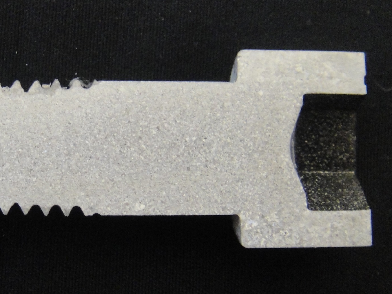 The macrography shows the longitudinal section of the allen bolt, 1/2" nominal diameter, that was machined from a heat treated bar (solution annealed and aged). The granular structure presents differences in the grain sizes.  At the bolt head (external surface of the original bar) the austenitic grain size is larger than in the center of the bar where the particles in segregated bands "arrested" the grains during hot forming and solution annealing.