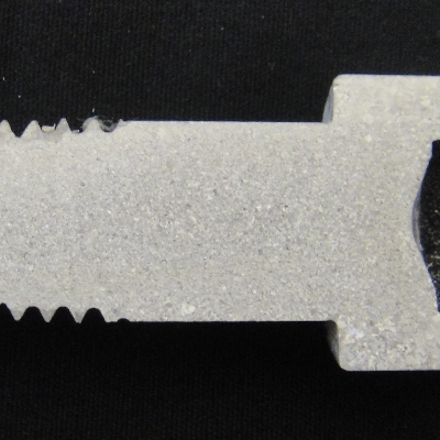 The macrography shows the longitudinal section of the allen bolt, 1/2" nominal diameter, that was machined from a heat treated bar (solution annealed and aged). The granular structure presents differences in the grain sizes.  At the bolt head (external surface of the original bar) the austenitic grain size is larger than in the center of the bar where the particles in segregated bands "arrested" the grains during hot forming and solution annealing.