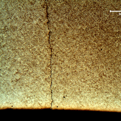 A micrography of the housing in a transverse section showing a through wall cracking, slightly branched and thin. The internal surface of the housing appears in the bottom of the figure.