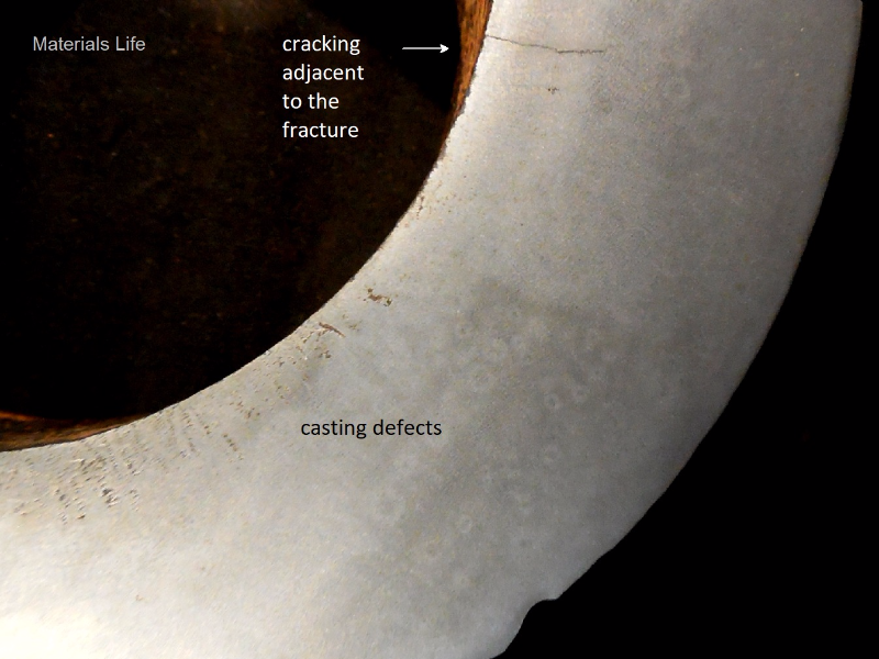 Macrography of a "longitudinal" section of the padeye showing casting defects close to the internal diamater and a secondary crack, paralel to fracture, starting from the internal diameter. The fracture is not presented in this macro, it is to the top of the photo.
