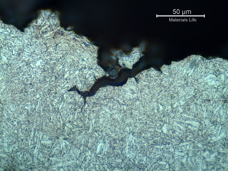 Micrographic detail of a transverse section, at the fracture (in the top of the figure).  The fracture is brittle and follows the voids at interdendritic spaces, with secondary cracks.