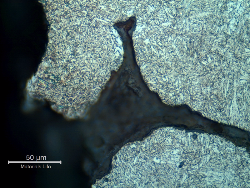Micrographic detail of a region with a large amount of casting defects. Shrinkage voids in interdendritic spaces, some interconnected and cracked. The microstructure is tempered martensite.