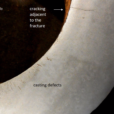 Macrography of a "longitudinal" section of the padeye showing casting defects close to the internal diamater and a secondary crack, paralel to fracture, starting from the internal diameter. The fracture is not presented in this macro, it is to the top of the photo.