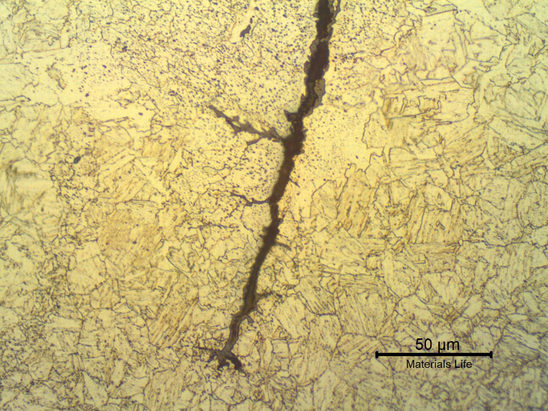 Micrographic detail of the forging lap defect that appears at the nut surface like a crack, filled with oxides.  The nut presented a martensitic structure in the center of the nut, but in the regions adjacent to the defect the structure is ferritic-bainitic due to decarburization.  There are several globular oxides (grey spots) that became entrapped during the forging.