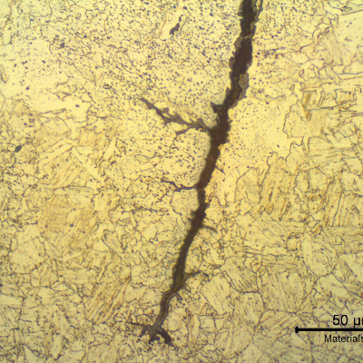 Micrographic detail of the forging lap defect that appears at the nut surface like a crack, filled with oxides.  The nut presented a martensitic structure in the center of the nut, but in the regions adjacent to the defect the structure is ferritic-bainitic due to decarburization.  There are several globular oxides (grey spots) that became entrapped during the forging.