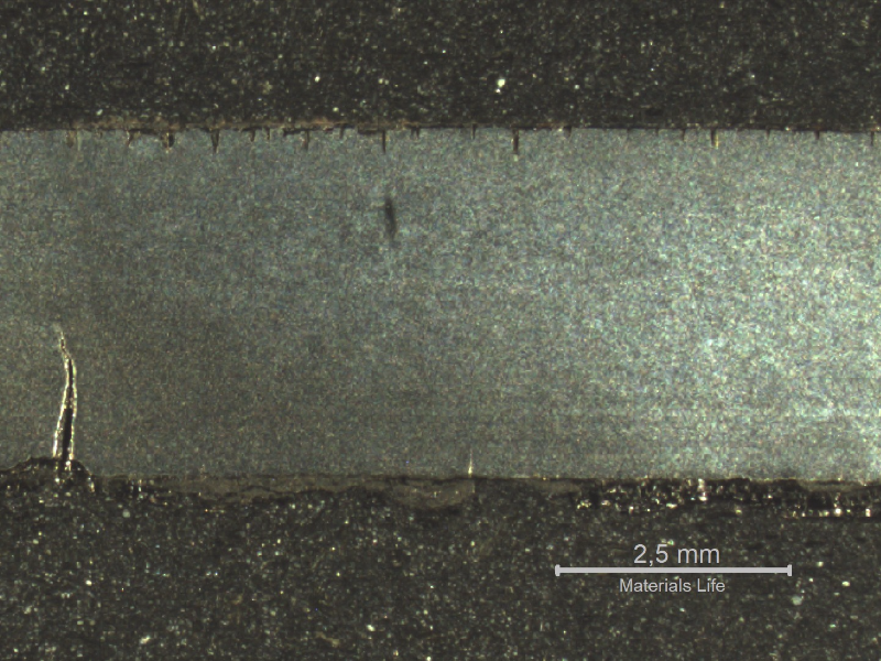 The macrography of a longitudinal section of the tube in the damaged area shows the circunferential cracks, from the internal and external sides of the tube. The outer diameter of the tube is in the top of the figure and the inner diameter is in the bottom of the figure.  From the outside there are several paralel cracks, as well as from the inner side.