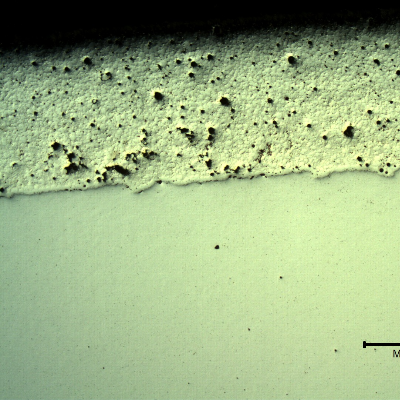 Micrography, as polished, of the transverse section of the forged pin with the layer applied by a (thermal) spray and fuse process.  The structure of the layer that is 0.7 mm thick, presented entrapped pores and globular oxides.  The layer was melted after application by thermal spray (in this case using a flame) and the pin was quenched and tempered after the full application and melting of the layer.