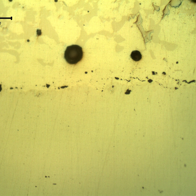 Micrographic detail, as polished, of the transverse section of the forged pin at the interface between the pin and the spray and fuse layer. The interface presents globular oxides and small pores, entrapped.