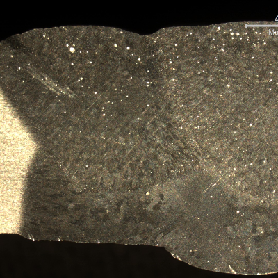 Macrographic detail of the flat position welded joint, showing the three passes.  The large extension of the heat affected zone in the root reveals the too high imposed energy, melting out of the root gap.  The shining spots are pores.