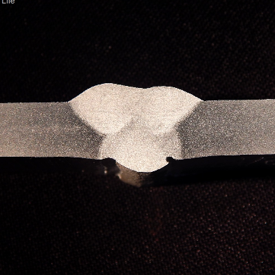 Macrography of the flat position welded joint. It was welded in three passes, with the following parameters.   
Root pass - 159A, 21V, 147mm/s (wire speed), 3.5 mm/s (welding speed), 979 J/mm.  
Second pass - 170A, 22V, 168mm/s (wire speed), 7.7 mm/s (welding speed), 538 J/mm.  
Third pass - 172A, 23V, 168mm/s (wire speed), 7.0 mm/s (welding speed), 587 J/mm.
