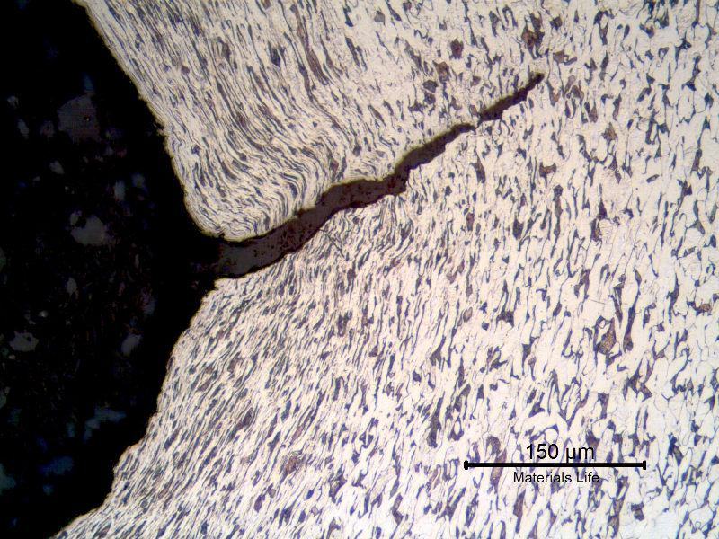Micrography of a longitudinal section of the bolt at the thread fillet adjacent to the fracture, presenting a ductile cracking from the bottom of the fillet, propagating with a strong plastic deformation.
The deformation lines of the cold formed process (thread cold rolling) are also deformed by the cracking propagation.