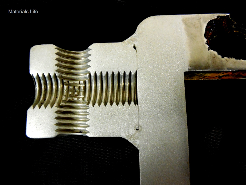 The macrography of a longitudinal section of the case shows one region where a through wall localized corrosion has occurred (in the left side of the image) and regions where the case was welded to a padeye, without any corrosion damage.