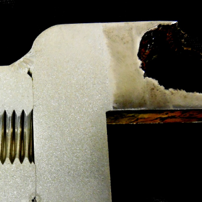 The macrography of a longitudinal section of the case shows one region where a through wall localized corrosion has occurred (in the left side of the image) and regions where the case was welded to a padeye, without any corrosion damage.