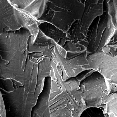 Fractographic detail of the longitudinal Charpy V testpiece,  broken at -46°C and presenting energy of 64J (the average energy of three tespieces was 70J).  The Charpy V testpiece was removed from the center of the bar. The micromechanism is quasicleavage and the test in this direction presented energy values superior than the minimum requirement of 45J.