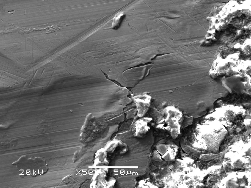SEM image showing a branching surface crack extending from a region of granular corrosion deposits into the polished substrate.