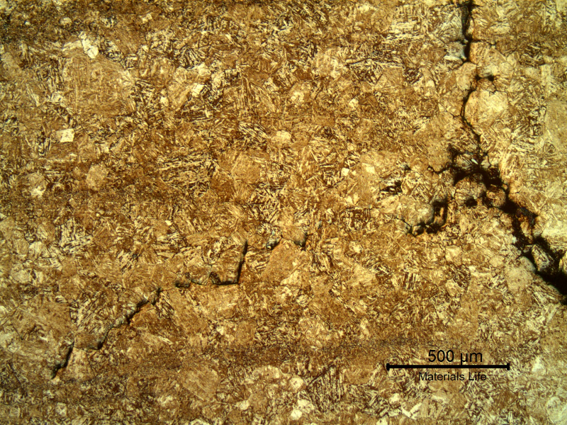 Micrograph showing a fine acicular martensitic matrix with a branching crack network, more extensive near the right edge.