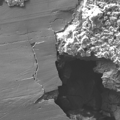 Higher magnification of the localized corrosion, showing that there are cracks at the margin of the corroded region.