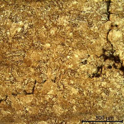 Micrograph showing a fine acicular martensitic matrix with a branching crack network, more extensive near the right edge.