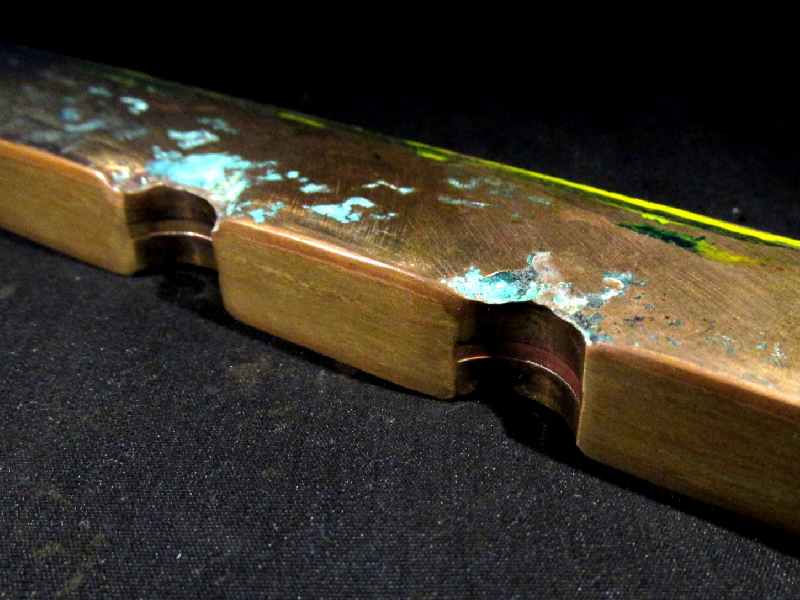 Transverse section of the tubesheet, after removal of the tubes.  The seawater sie is to the top of the figure.  It is possible to see regions of localized corrosion close to the tube position and a red layer all through the plate surface.