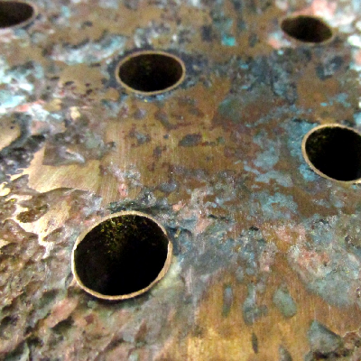 Aspect of the CuZn platesheet where it is corroded (cooling medium side).  The (hot) air cooler uses treated seawater as the cooling medium and the corroded regions are associated to the regions in the heat exchanger of higher temperatures, and the leakage occurred in regions of contact of the platesheet to cooper alloy tubes.