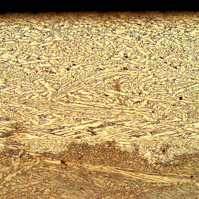 Same region of the previous figure, after etching. Micrography presenting the interface between the layer where the dezincification occurred (top of the figure) and the region where the material was not yet corroded (bottom of the figure, now etched to reveal the microstructure).