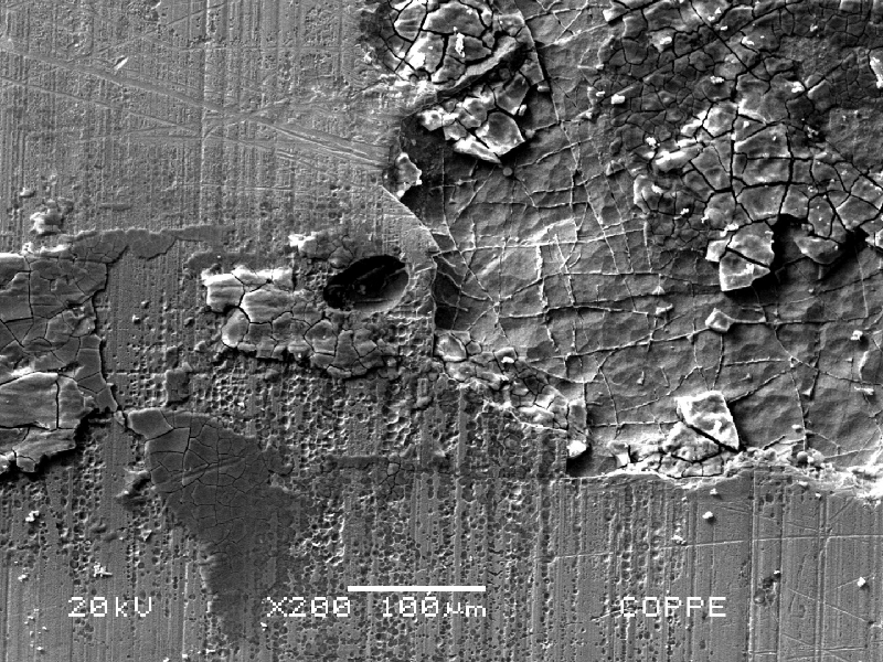 Scanning electron microscopy image of the chromium plated cylinder surface, presenting deposits and localized dissolution under deposits. There are different stages of corrosion in this region, observed in low magnification. Small areas of attack and a shallow pitting with deposits that were analyzed by EDS and revealed the presence of S.