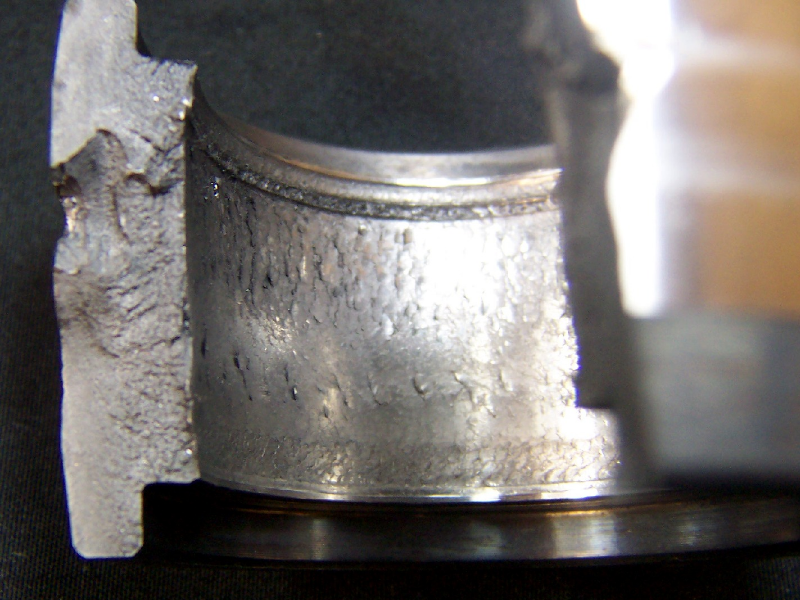 Aspect of the broken cylindrical roller bearing, presenting the internal diameter full of cracks; and the fracture revealing two different morphologies, flat and smooth close to the external diameter (that appeared white in the macrography); and rough close to the internal diameter (that appeared dark in the macrography).