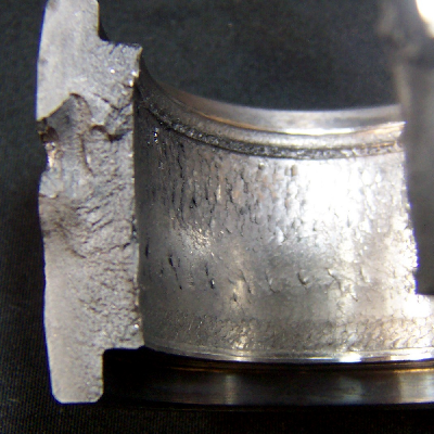 Aspect of the broken cylindrical roller bearing, presenting the internal diameter full of cracks; and the fracture revealing two different morphologies, flat and smooth close to the external diameter (that appeared white in the macrography); and rough close to the internal diameter (that appeared dark in the macrography).