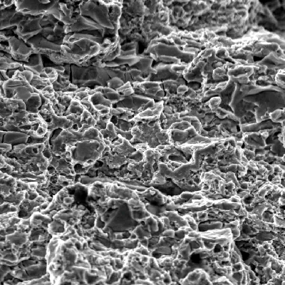 Fracture micromechanism at a region close to the external surface.  In this position the fracture shows quasecleavage, as well as decohesion of large carbides. typical of overloading this high strenght martensitic structure (64 HRc).