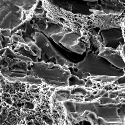 Aspect of the roller bearing fracture surface, by scanning electron microscopy, close to the internal surface.  In this position the fracture shows ductile micromechanisms (dimples) as well as decohesion of large carbides and (brittle) cleavage facets, typical of overloading this low strenght, and low toughness, ferritic structure (21 HRc).  The structure in this region, ferritic with large broken carbides and small rounded carbides, is of a low toughness, as indicated by the fracture.