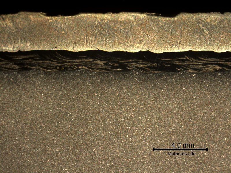 The macrography of a longitudinal section shows the low alloy (C-Mn) steel pipe, internally cladded by overlay in two layers.