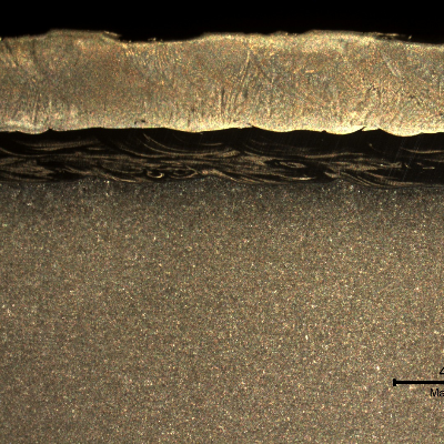 The macrography of a longitudinal section shows the low alloy (C-Mn) steel pipe, internally cladded by overlay in two layers.