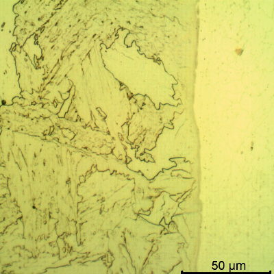 Micrographic detail of a longitudinal section of the pipe at the interface with the clad plate, with Nital etch that reveals only the low alloy steel structure, to the left side of the image. The metallurgical bonding of the claded plate to the substrate is evident since there are no voids or defects.