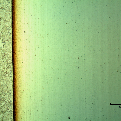 Low magnification micrography of a longitudinal section of the pipe at the interface with the clad plate, with electrolytic etch that reveals the clad plate structure (to the right side of the image), as well as the clad interface.
