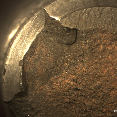 Macroscopic view of the fracture surface showing that there is a flat appearance of the fracture close to the bottom of the thread (upper side of the figure) and a flat, but rough appearance in the center of the stud. No evidences of corrosion in the thread fillets indicating that the stud was protected.