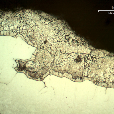 Micrographic detail of the section transverse to the fracture (top of the figure), suggesting the intergranular morphology (at the previous austenite grain boundaries) and the deposits of zinc over the fracture that create a condition of protection of the base metal during the metallographic etch, and the material is not fully etched.