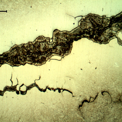 Micrographic detail of the secondary intergranular cracks, filled with zinc. The zinc appears dark because of the Nital etch, and the steel is not fully revealed because of the protection by the zinc.