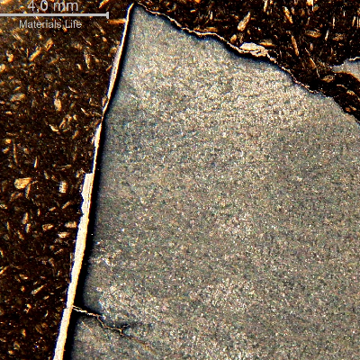 Macrography of a section transverse to the fracture, at the surface of the casting. It is possible to see the large thickness of the galvanized layer at the surface (left side of the figure). There is a white layer over the fracture surface (top of the figure) and branch cracks starting from the surface, parallel to the fracture (in the bottom left side of the figure).