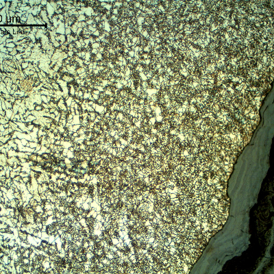 Micrography of the pipe at the leakage position showing an oxide layer inside the crevice.  The corrosion occurred exactly at the weld metal and the region at the margin of the damage shows the heat affected zone of the autogenous weld, with a refined grain size.