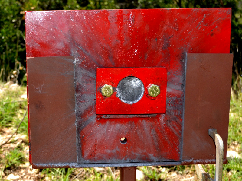 Red painted device where the 50 mm x 50 mm high strenght wear resistant steel plate (AR500) was positioned (in the circle). The image presents the target, positioned 100 meters far from the gun, after the shot and the projectile did not penetrate in the plate, and not even affected the material surface, as will be presented in the other figures.