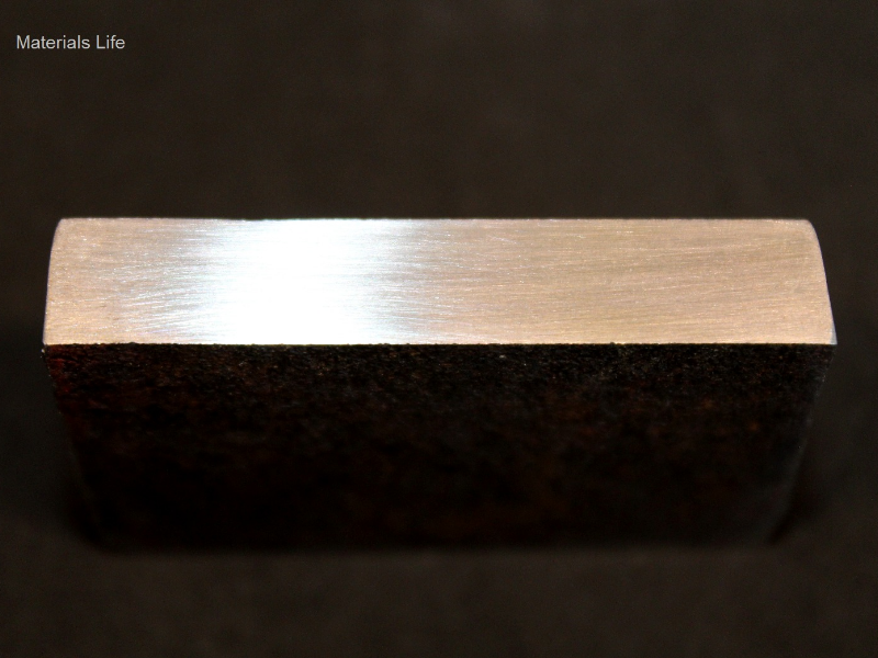 Aspect of the 3/8" thickness plate, 50 mm x 50 mm, of the AR500 wear resistant steel, in a section transverse to the impact position evidencing lack of plastic deformation, or any other damage. The impact surface is to the top of the figure.